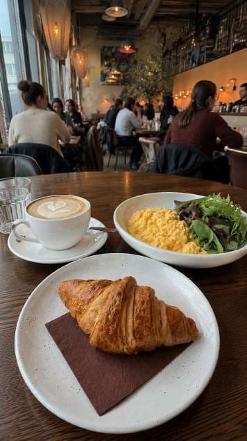 AI render in a candid style: croissant and coffee in a busy dining room