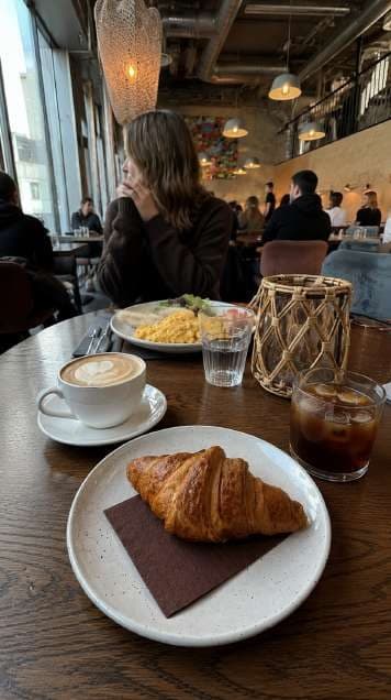 AI render in a candid style: croissant and coffee with diners in the background