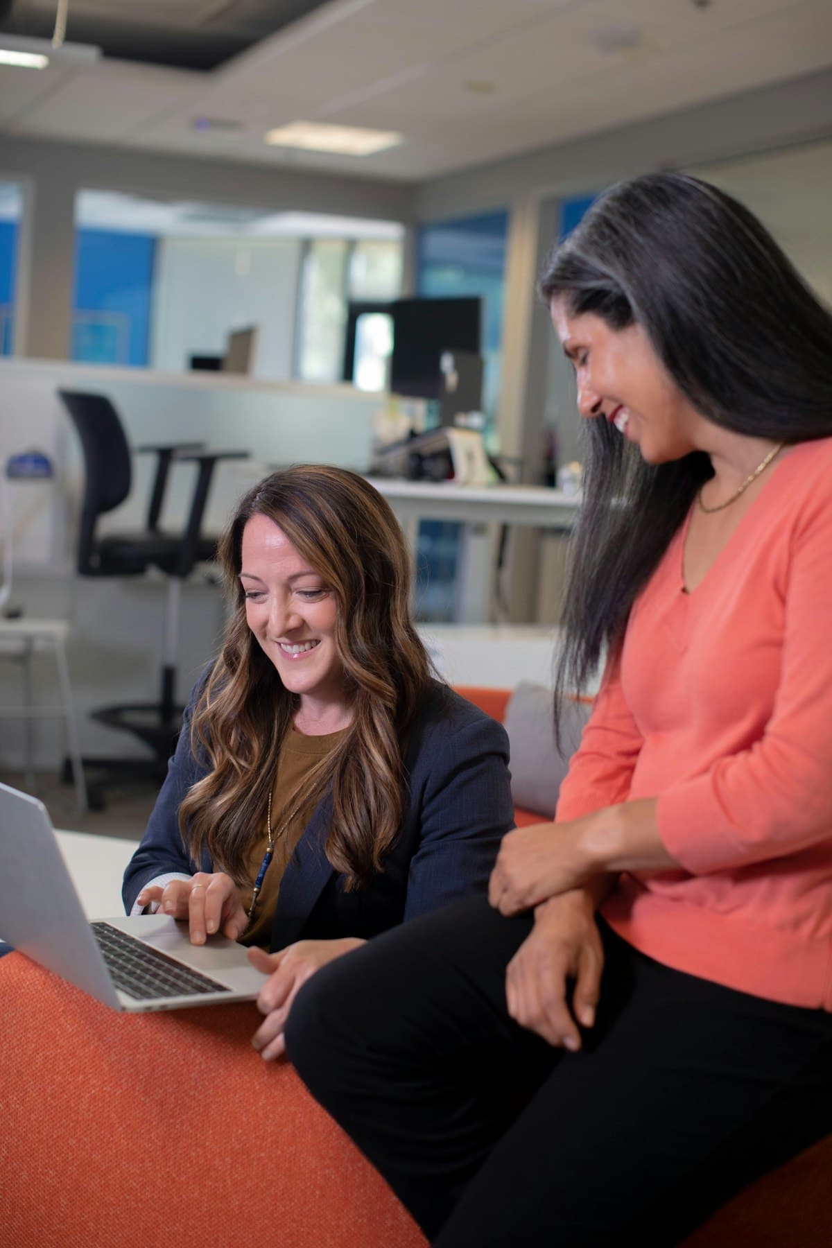 Two colleagues laughing together over a laptop in a bright office