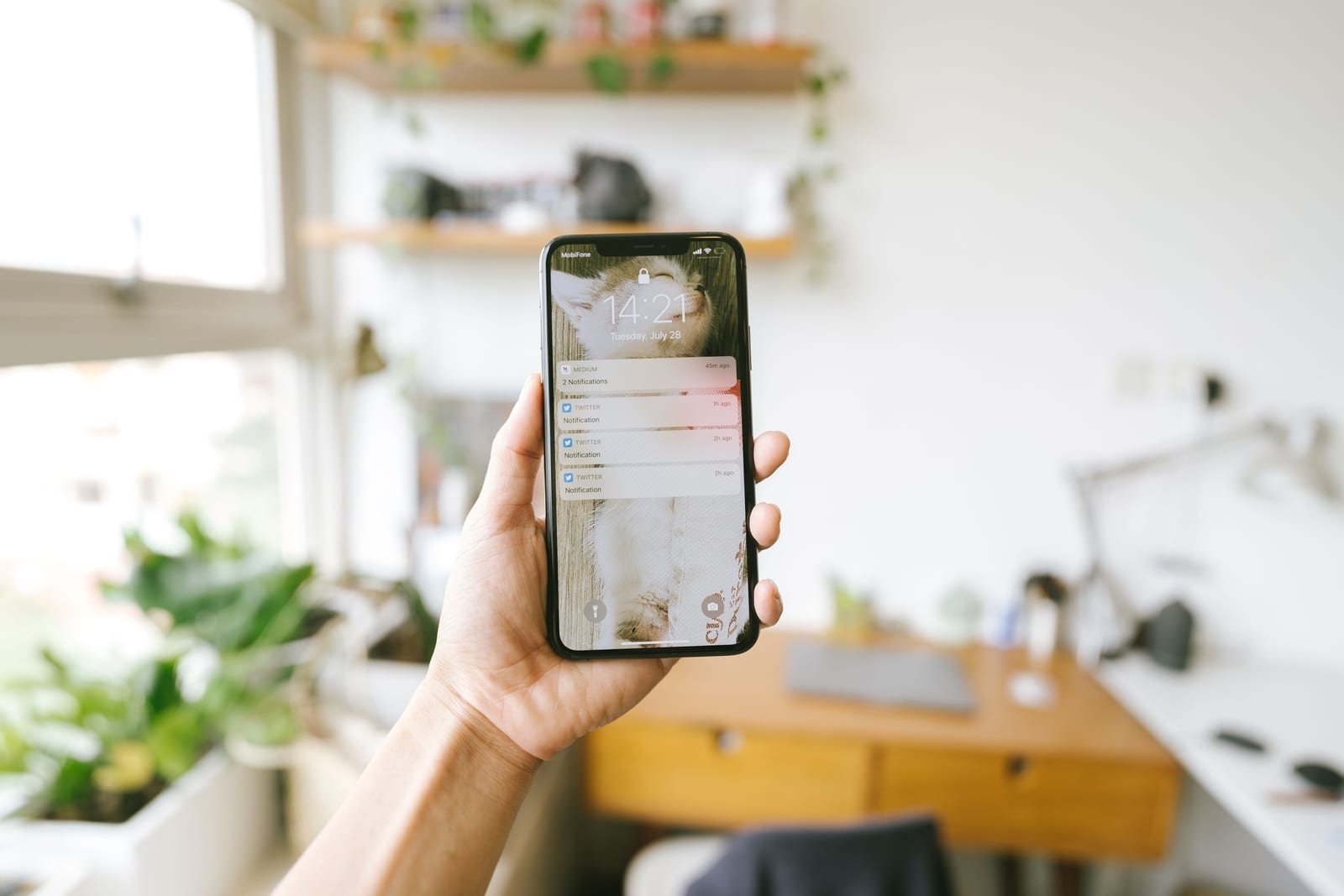 Hand holding a smartphone above a desk with a laptop nearby