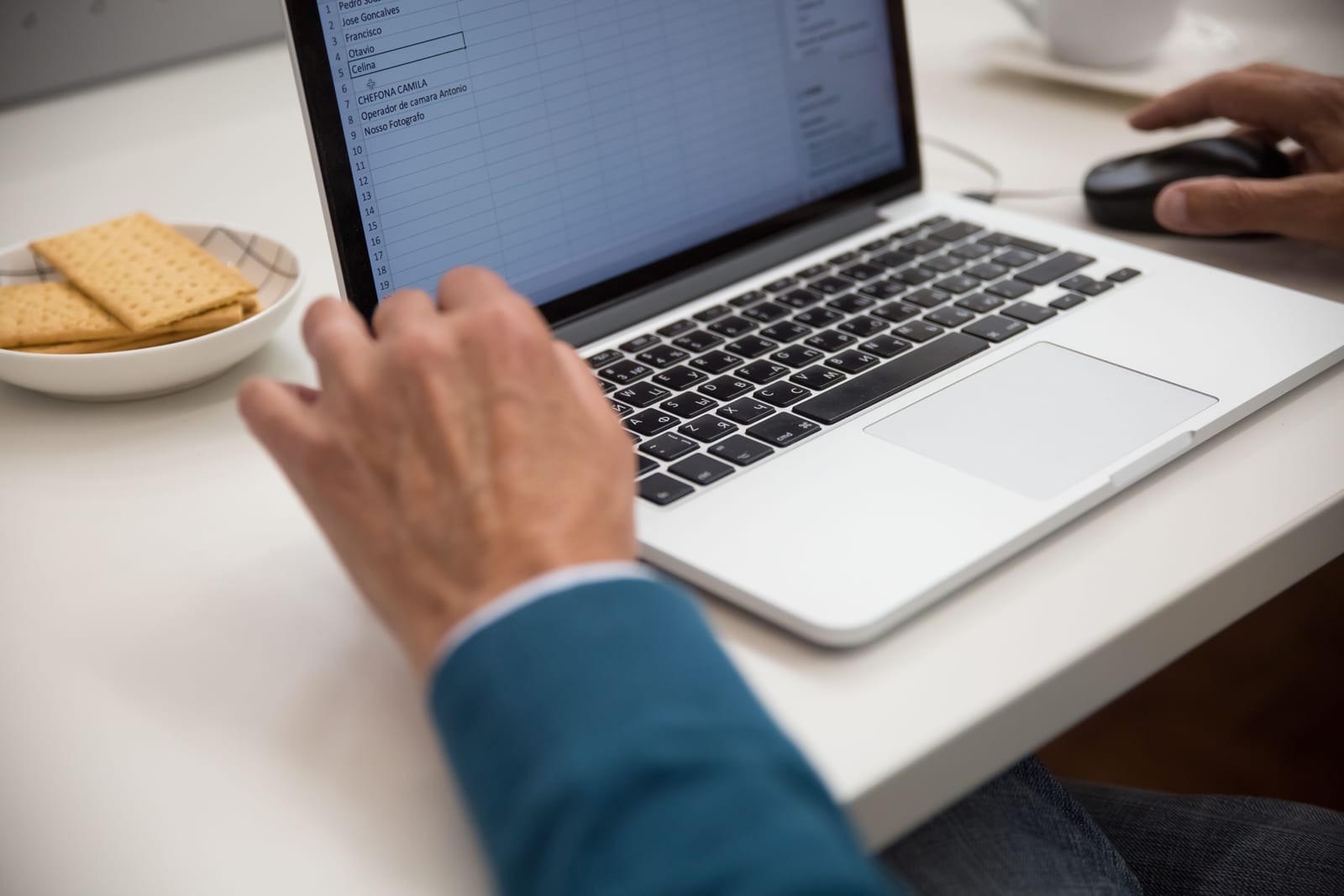 Hands typing on a laptop showing a spreadsheet with rows of data