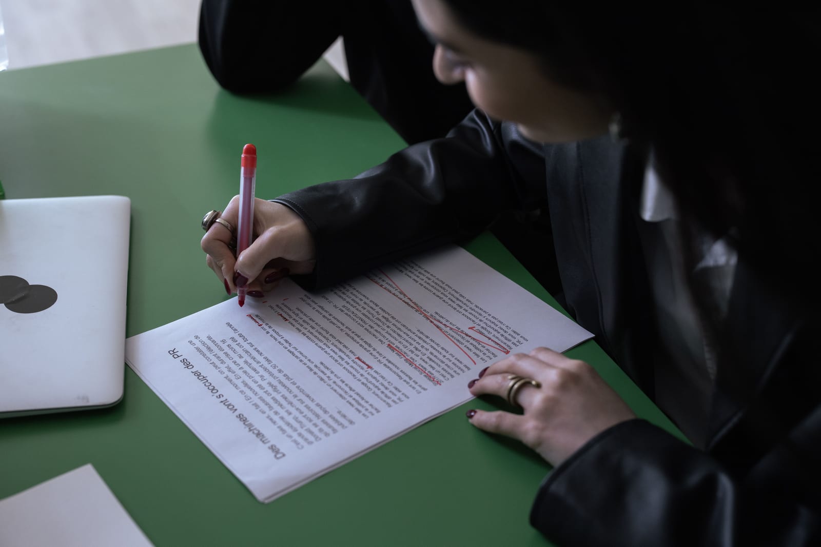 Person editing a document on a laptop at a desk with a pen nearby